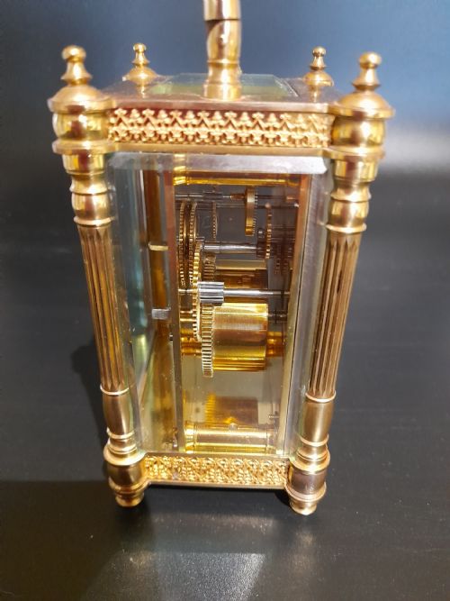 fig 3. A gilded brass carriage clock featuring clear glass side panels, turned corner columns, a folding top handle, and a white enamel dial with Arabic numerals.