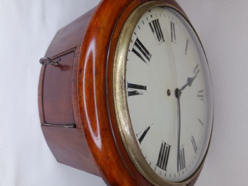 fig 1. A circular Victorian wall clock featuring a turned mahogany wooden case, a brass glass bezel, and a white dial with black Roman numerals.