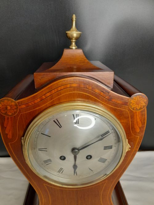 fig 1. An Art Nouveau satinwood mantel clock featuring floral marquetry inlays, a silvered Roman numeral dial, a brass finial, and brass bracket feet.