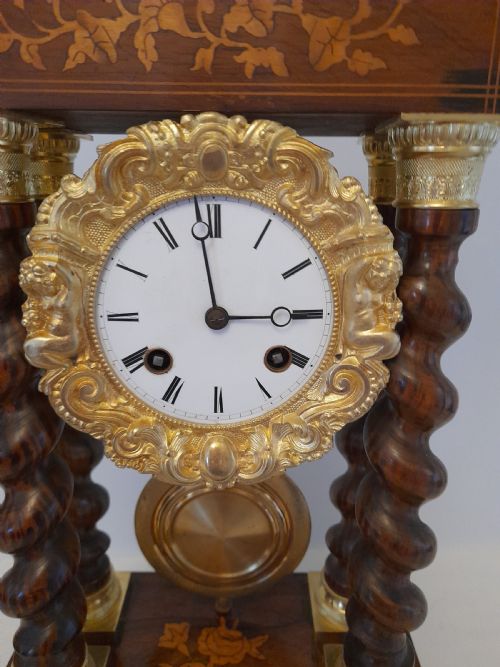 fig 1. A 19th-century French rosewood portico clock featuring twisted columns, floral marquetry inlays, a white enamel dial with Roman numerals, and a gilt metal pendulum.