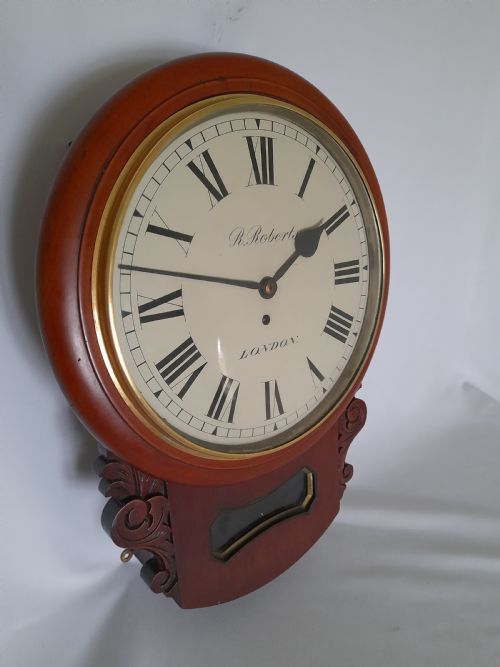 fig 1. A Victorian mahogany drop-dial wall clock featuring a brass-rimmed cream dial with Roman numerals, black spade hands, and carved scrollwork details on the lower case.