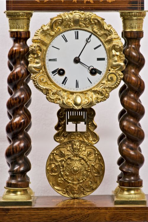 fig 1. A 19th-century rosewood portico clock featuring floral marquetry inlays, twin barley-twist columns with gilt capitals, and a white enamel dial with an ornate gilt bezel.