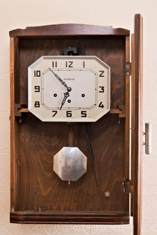 fig 1. An Art Deco rectangular wooden wall clock featuring a light octagonal dial with Arabic numerals above a geometric leaded glass window.