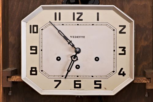 fig 2. An Art Deco rectangular wooden wall clock featuring a light octagonal dial with Arabic numerals above a geometric leaded glass window.