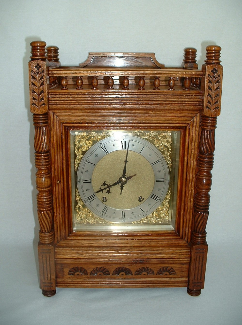 An antique carved oak bracket clock featuring a brass dial with Roman numerals, side columns, and decorative balustrade top gallery.