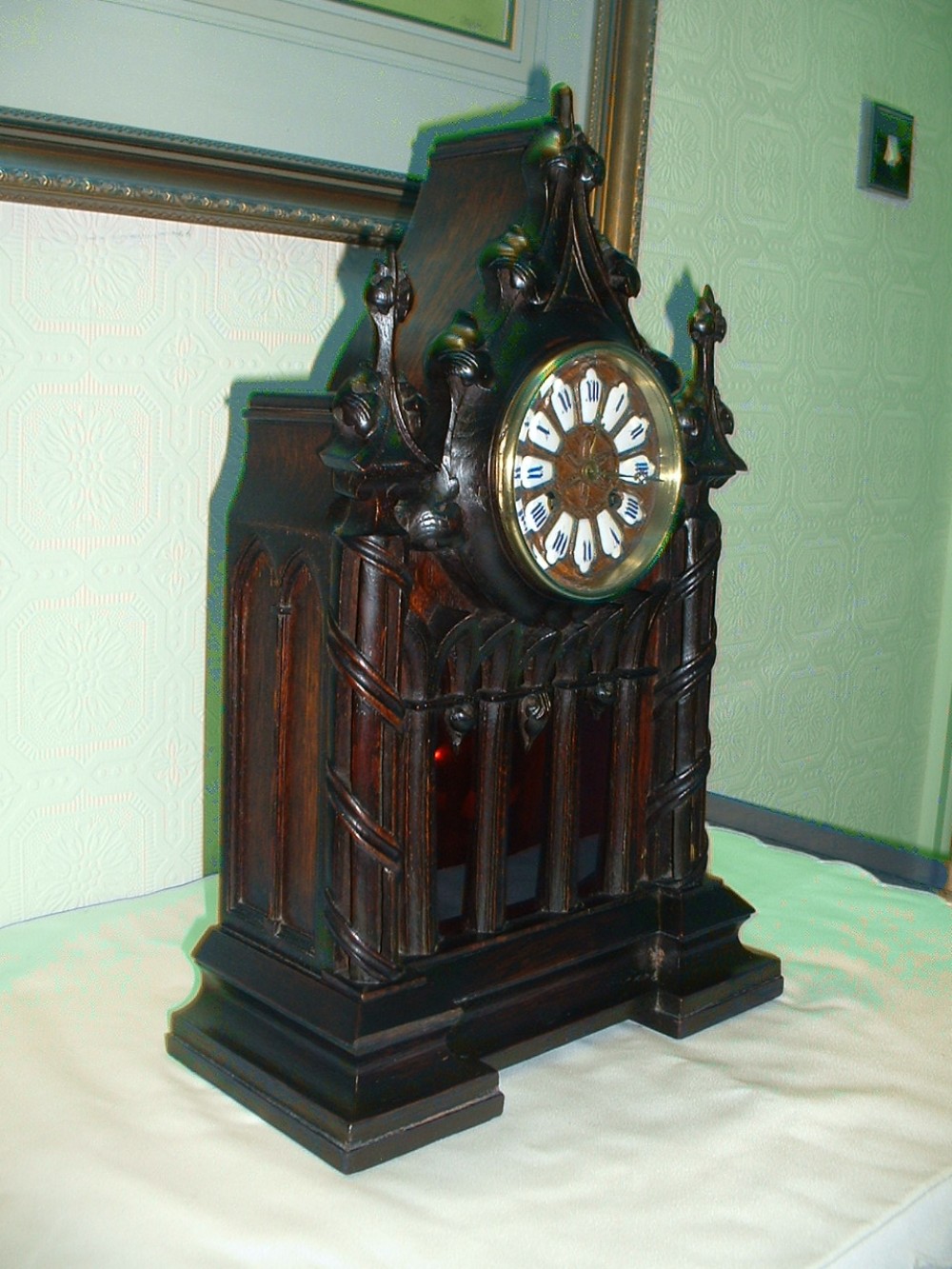 A dark carved wooden bracket clock featuring Gothic architectural arches, decorative spires, twist columns, and a brass dial with white enamel hour markers.
