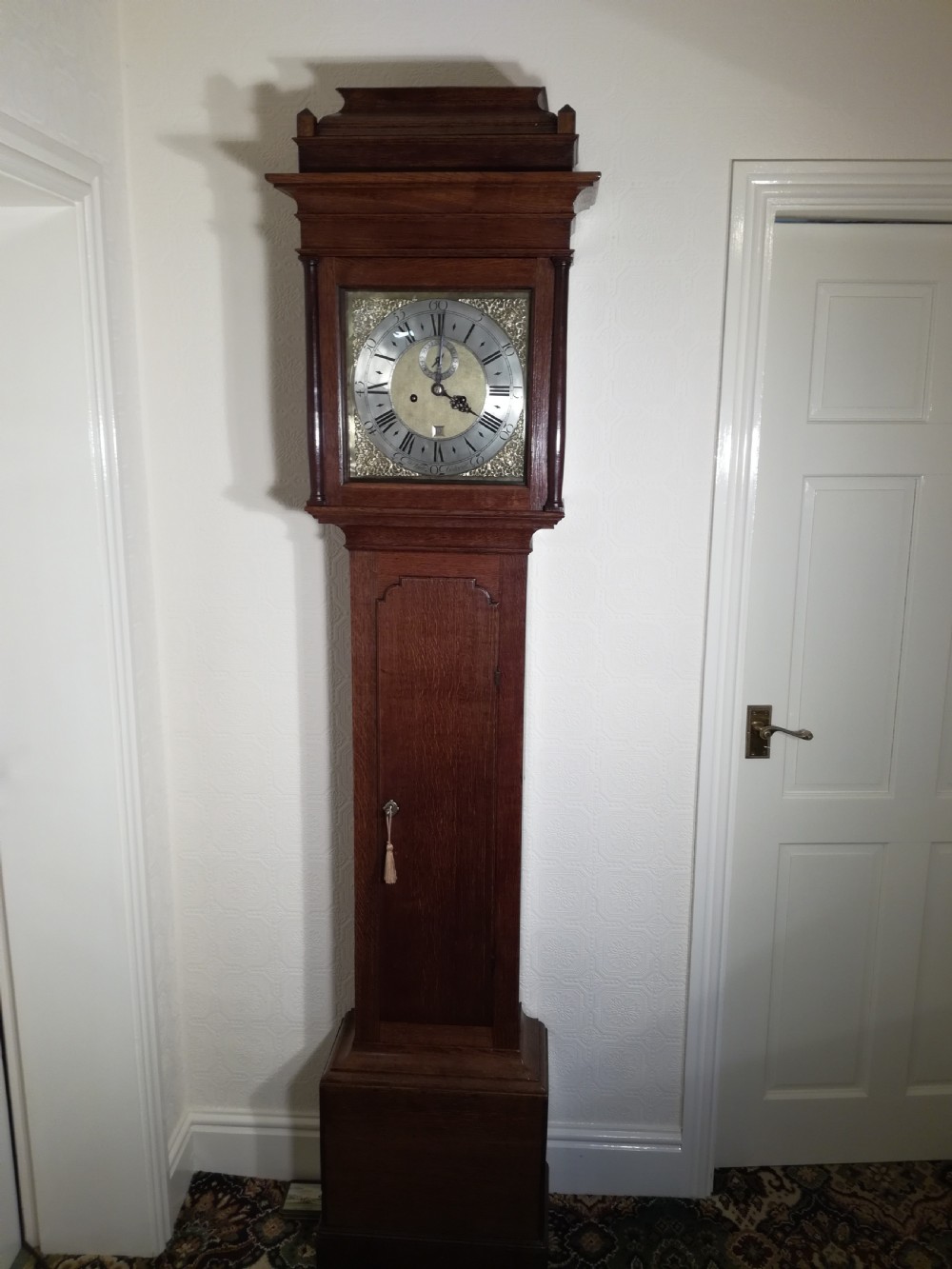 An 18th-century Georgian dark oak longcase clock featuring a square brass dial with decorative corner spandrels and a moulded hood.