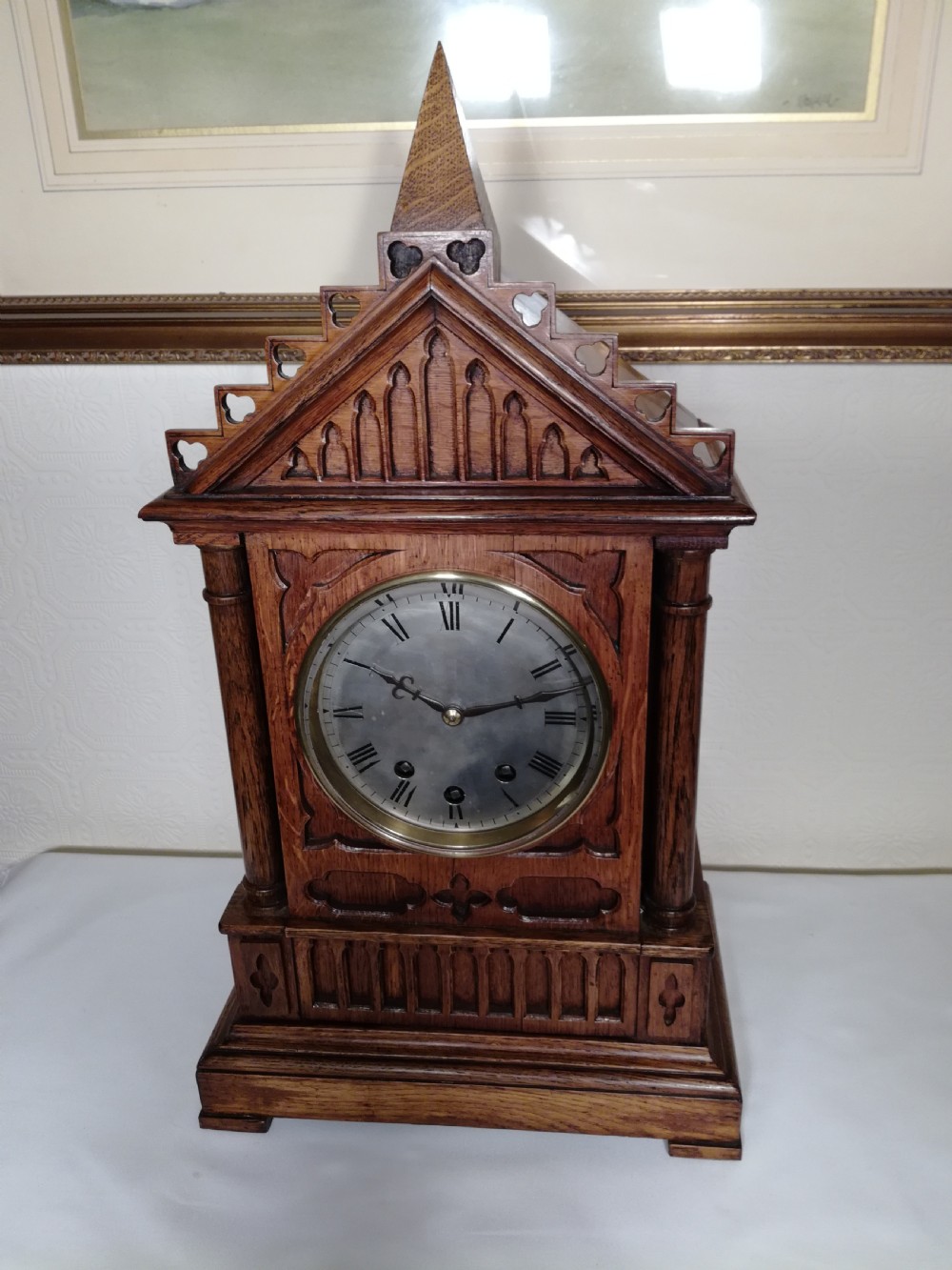 A Victorian Gothic Revival carved oak bracket clock featuring a cathedral arch pediment with spire, blind tracery carving, corner columns, and a silvered dial with Roman numerals.
