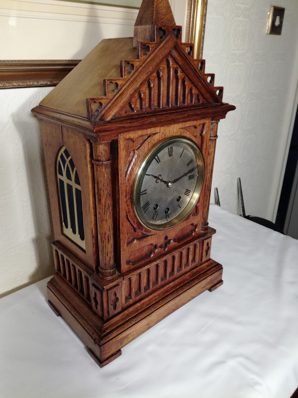 A Victorian Gothic Revival carved oak bracket clock featuring a cathedral arch pediment with spire, blind tracery carving, corner columns, and a silvered dial with Roman numerals. View V