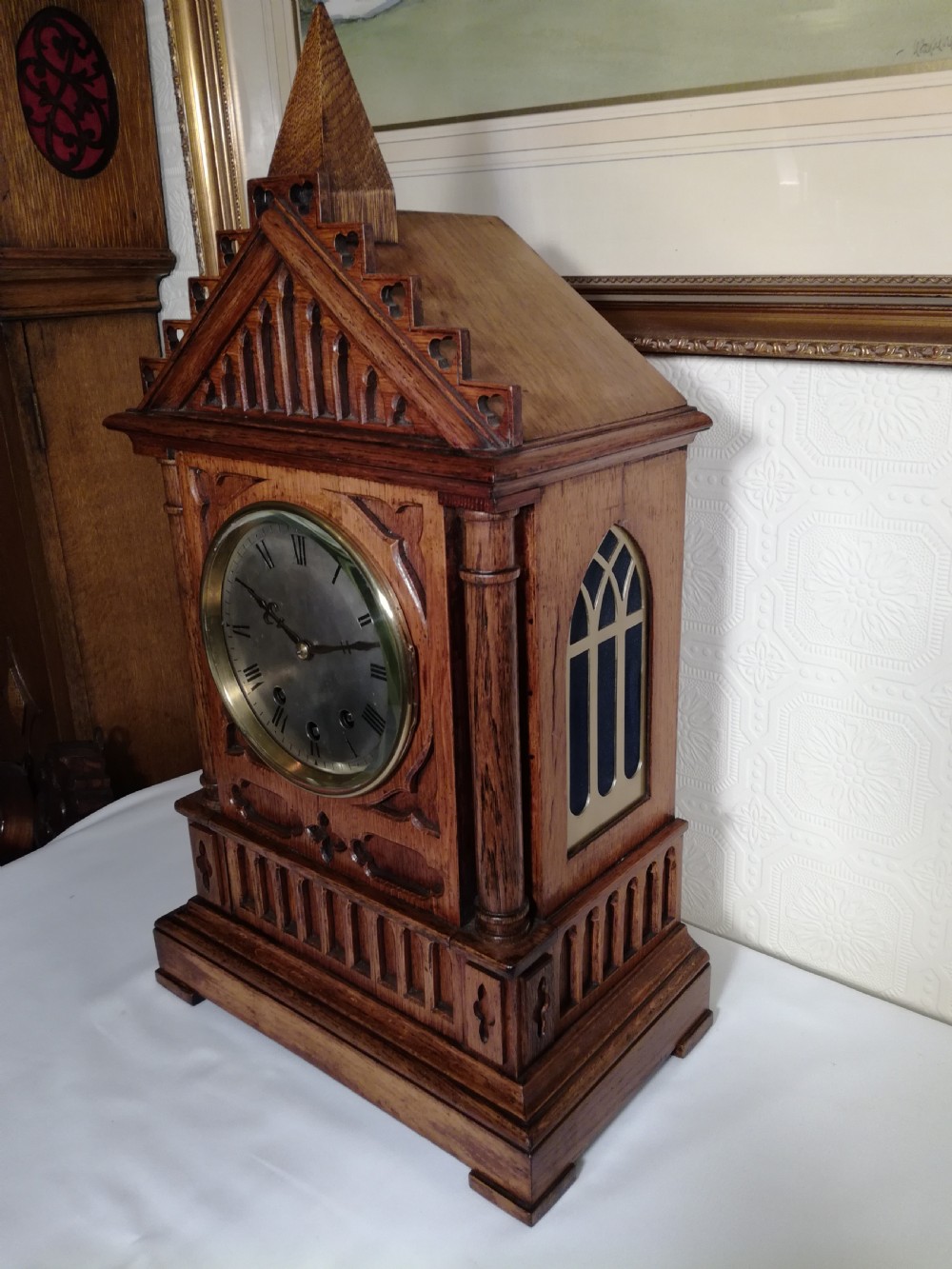A Victorian Gothic Revival carved oak bracket clock featuring a cathedral arch pediment with spire, blind tracery carving, corner columns, and a silvered dial with Roman numerals. View VI