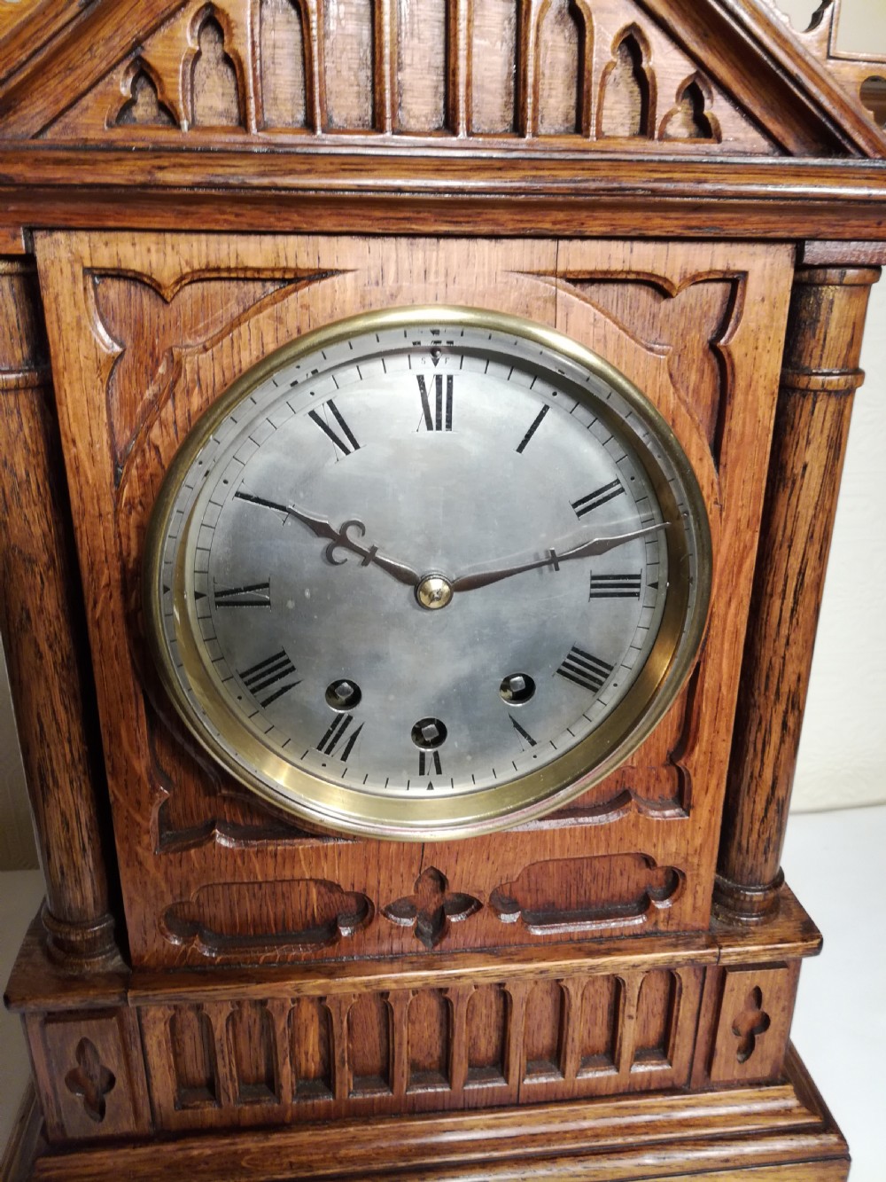 A Victorian Gothic Revival carved oak bracket clock featuring a cathedral arch pediment with spire, blind tracery carving, corner columns, and a silvered dial with Roman numerals. View VII