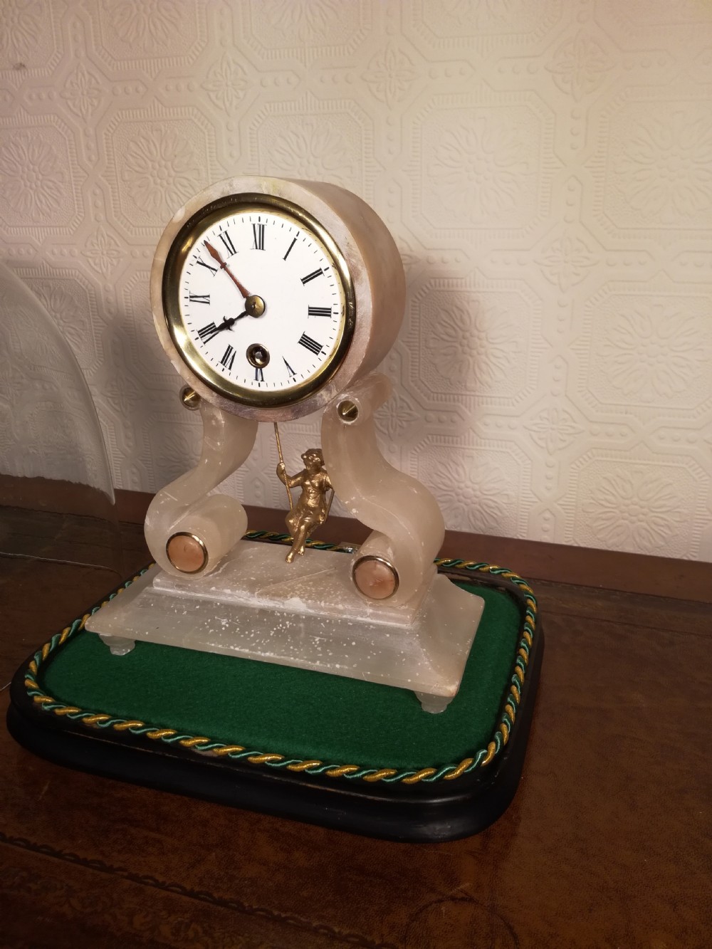An antique French alabaster mantel clock under a clear glass dome, featuring a circular white dial above a gilt cherub figure on a swing pendulum. View VII