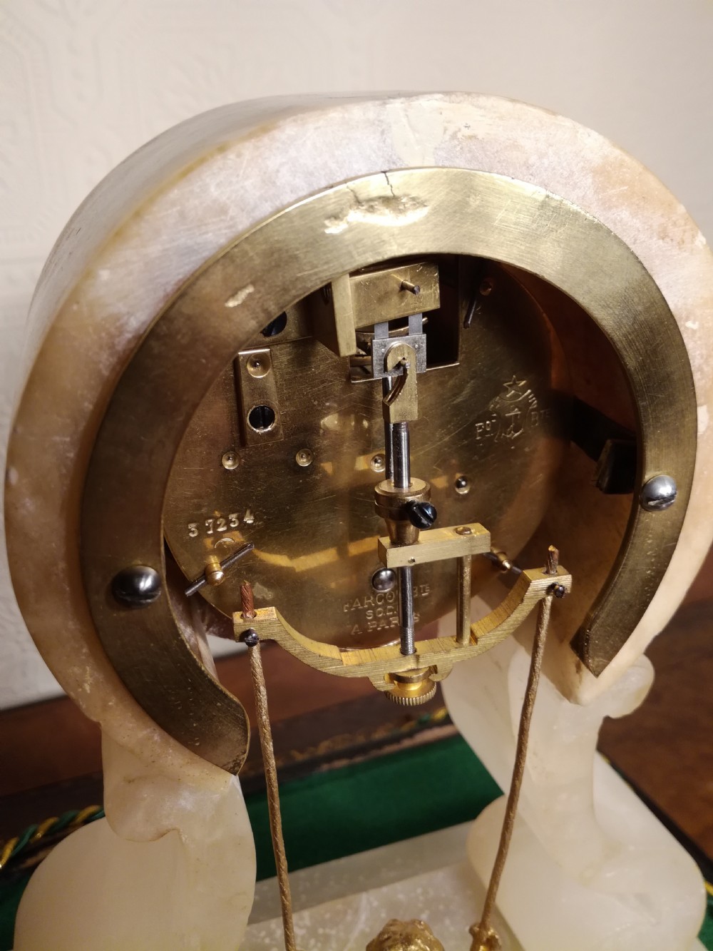 An antique French alabaster mantel clock under a clear glass dome, featuring a circular white dial above a gilt cherub figure on a swing pendulum. View VIII