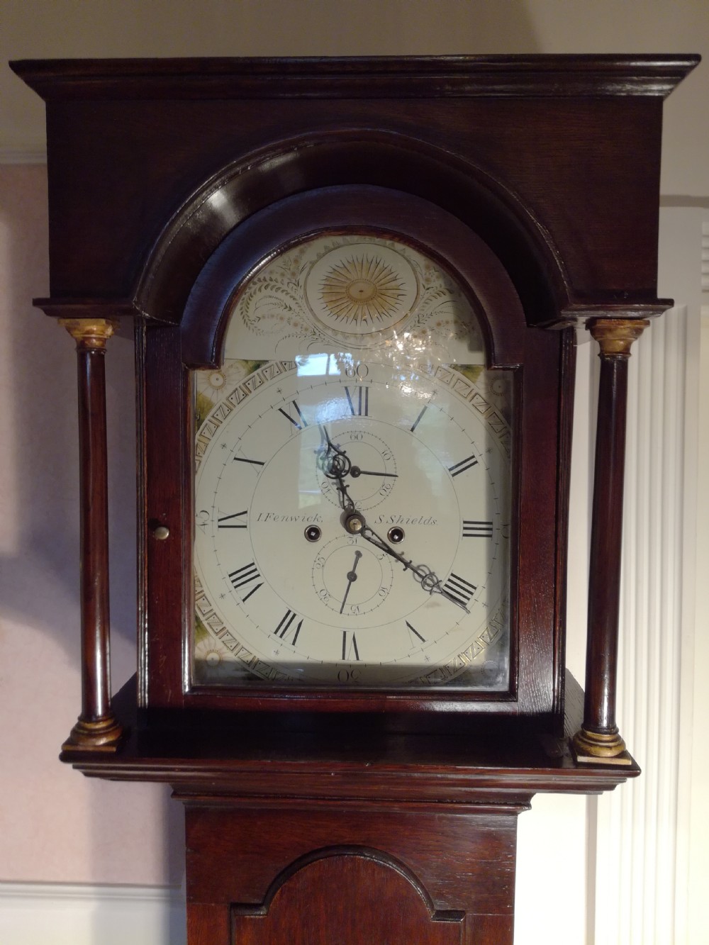 A Georgian dark mahogany longcase clock featuring an arched dial hood with turned columns and a tall waist door. View X