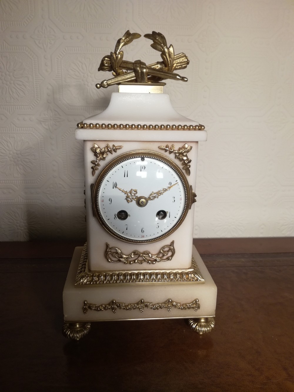 A French Louis XVI style white marble mantel clock featuring gilt bronze mounts, a laurel wreath finial, and an enamel dial.