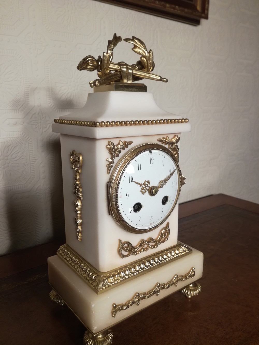 A French Louis XVI style white marble mantel clock featuring gilt bronze mounts, a laurel wreath finial, and an enamel dial. View V