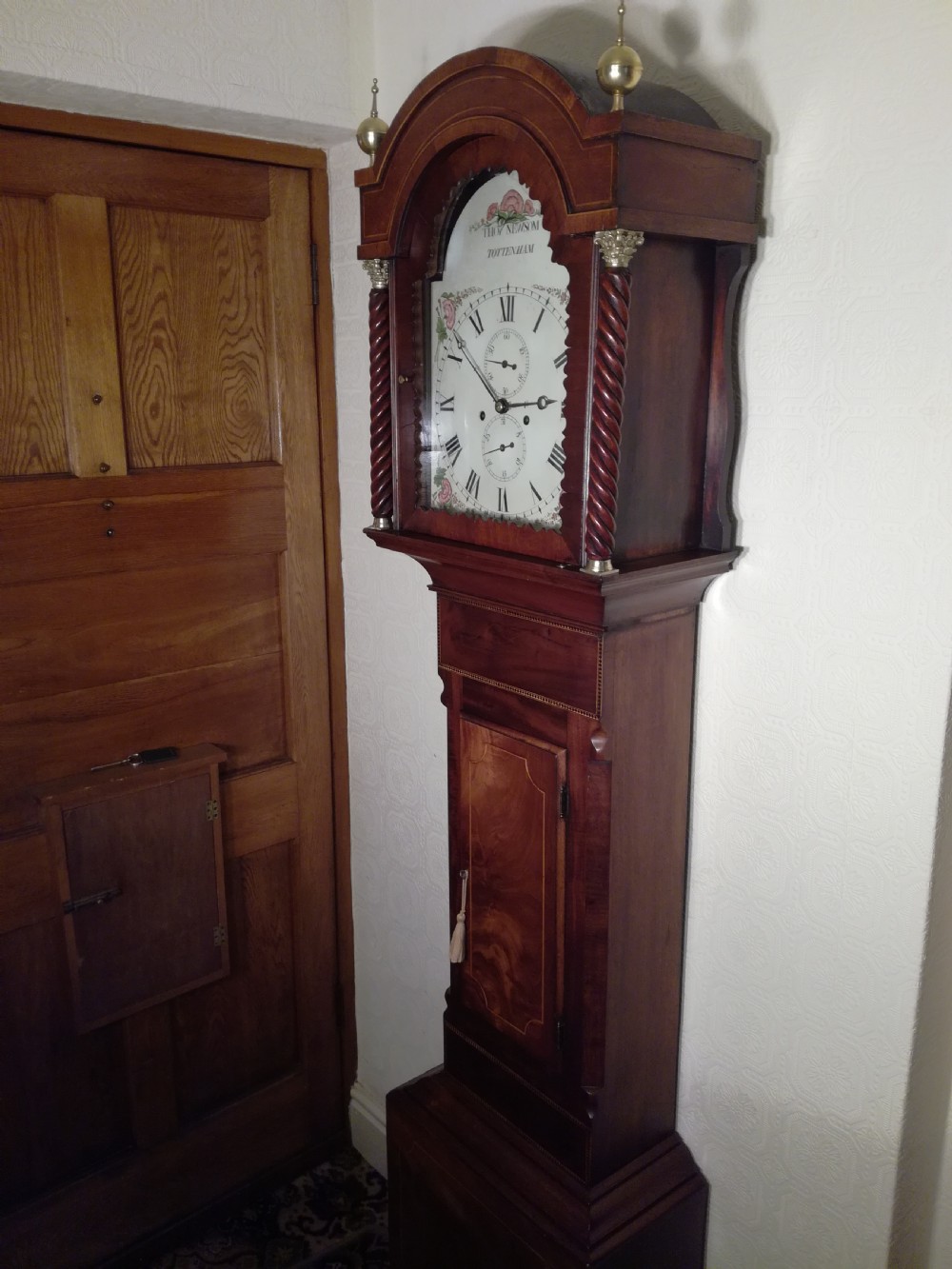 A tall Regency flame mahogany longcase clock featuring brass ball finials, spiral twisted columns flanking the hood, and an arched painted dial with Roman numerals.
