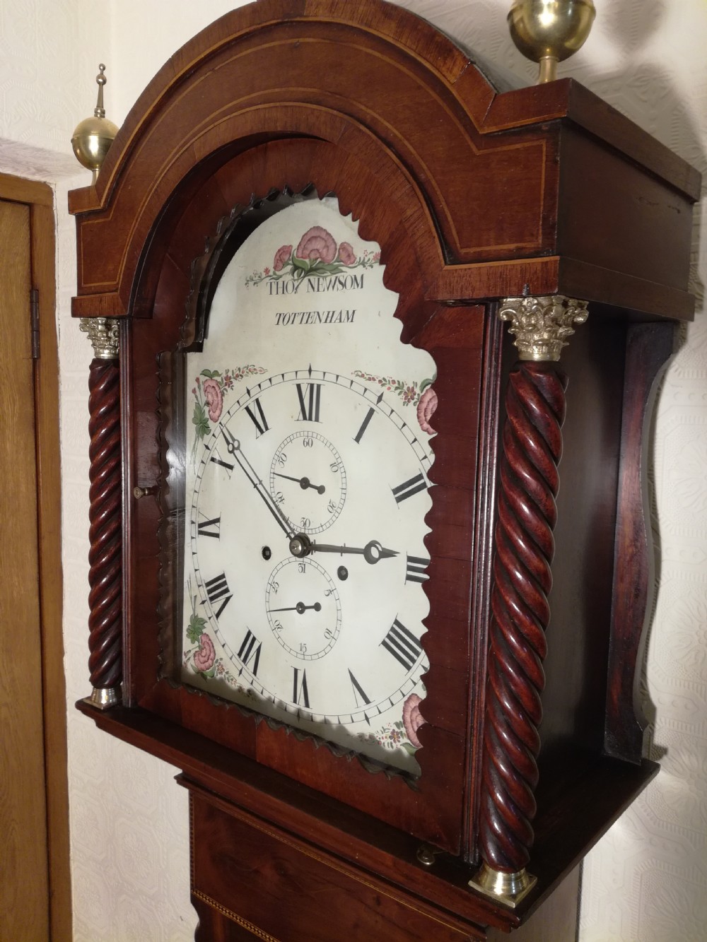 A tall Regency flame mahogany longcase clock featuring brass ball finials, spiral twisted columns flanking the hood, and an arched painted dial with Roman numerals. View II