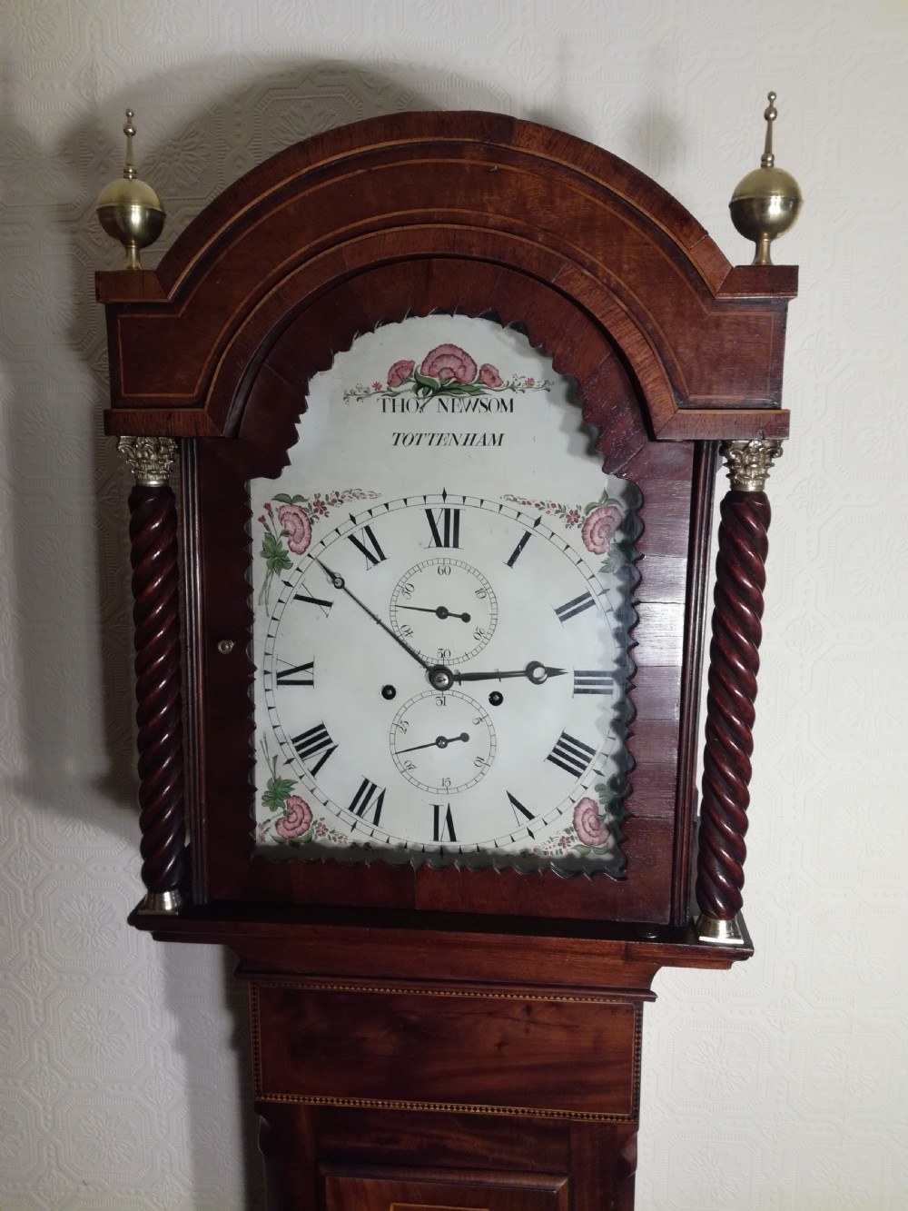 A tall Regency flame mahogany longcase clock featuring brass ball finials, spiral twisted columns flanking the hood, and an arched painted dial with Roman numerals. View III