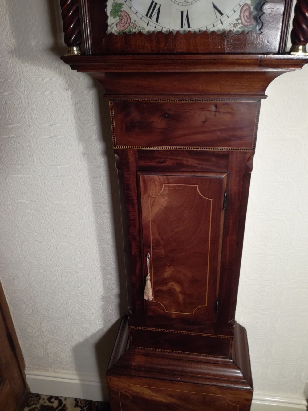 A tall Regency flame mahogany longcase clock featuring brass ball finials, spiral twisted columns flanking the hood, and an arched painted dial with Roman numerals. View V