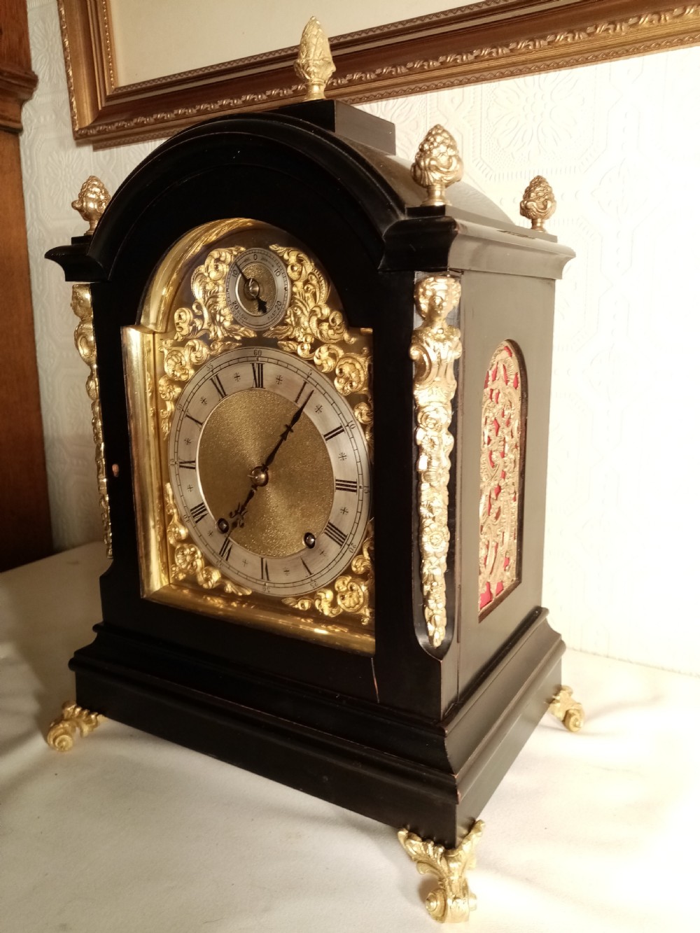 A Victorian ebonised bracket clock featuring gilt brass caryatid mounts, pinecone finials, scroll feet, and a brass dial with silvered chapter ring.