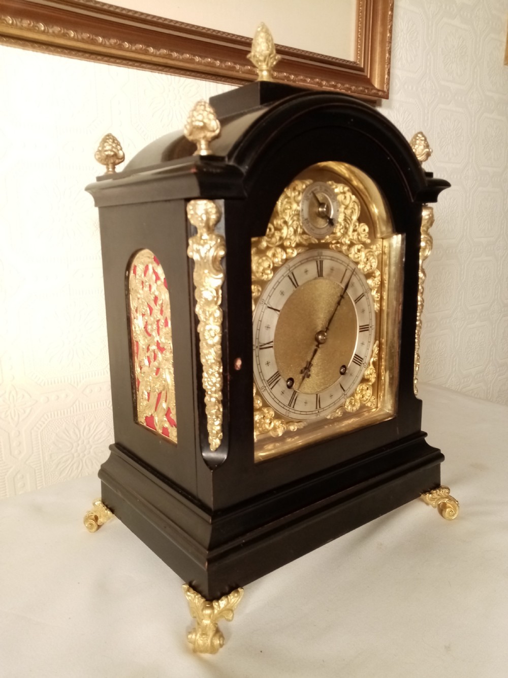 A Victorian ebonised bracket clock featuring gilt brass caryatid mounts, pinecone finials, scroll feet, and a brass dial with silvered chapter ring. View II