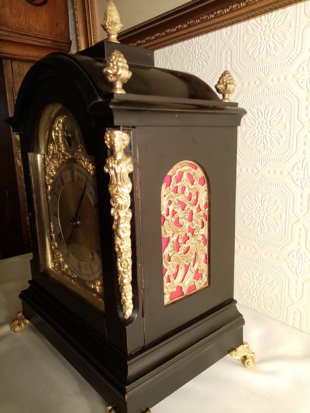 A Victorian ebonised bracket clock featuring gilt brass caryatid mounts, pinecone finials, scroll feet, and a brass dial with silvered chapter ring. View V