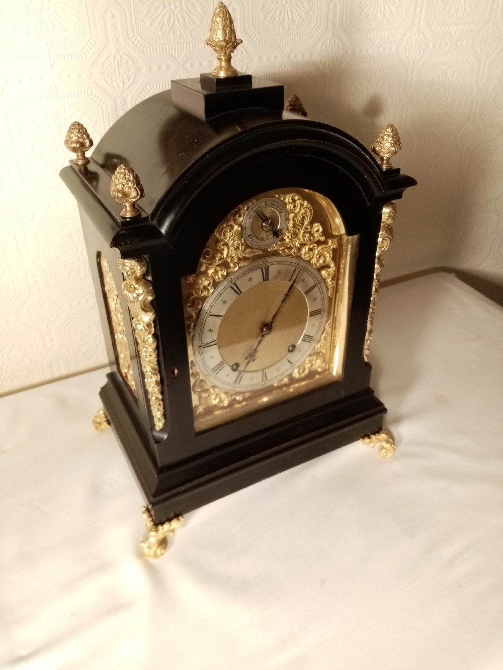 A Victorian ebonised bracket clock featuring gilt brass caryatid mounts, pinecone finials, scroll feet, and a brass dial with silvered chapter ring. View VI