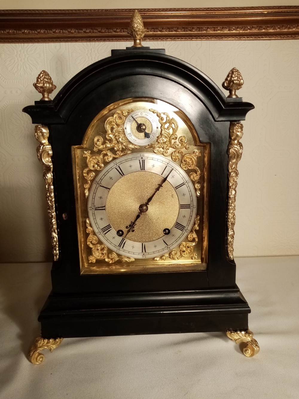 A Victorian ebonised bracket clock featuring gilt brass caryatid mounts, pinecone finials, scroll feet, and a brass dial with silvered chapter ring. View VII