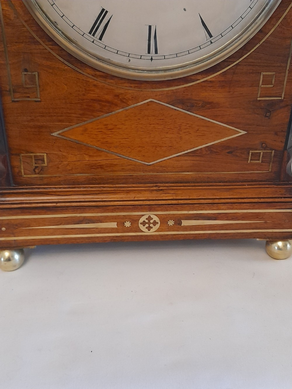 A Regency period rosewood bracket clock featuring geometric brass inlay, arched top with brass handle, gothic side frets, circular dial, and brass ball feet. View III
