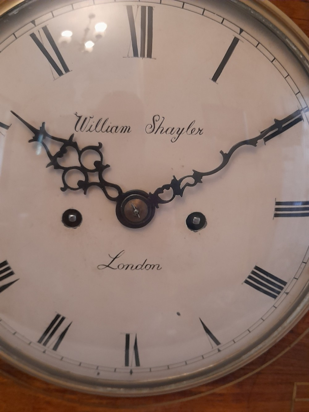 A Regency period rosewood bracket clock featuring geometric brass inlay, arched top with brass handle, gothic side frets, circular dial, and brass ball feet. View V