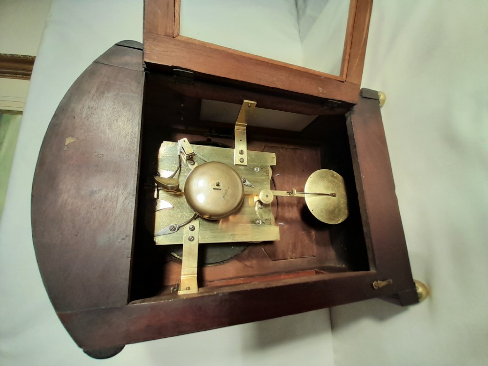 A Georgian mahogany bracket clock featuring brass inlay decoration, carved foliage cresting, and a white circular dial with Roman numerals. View VI