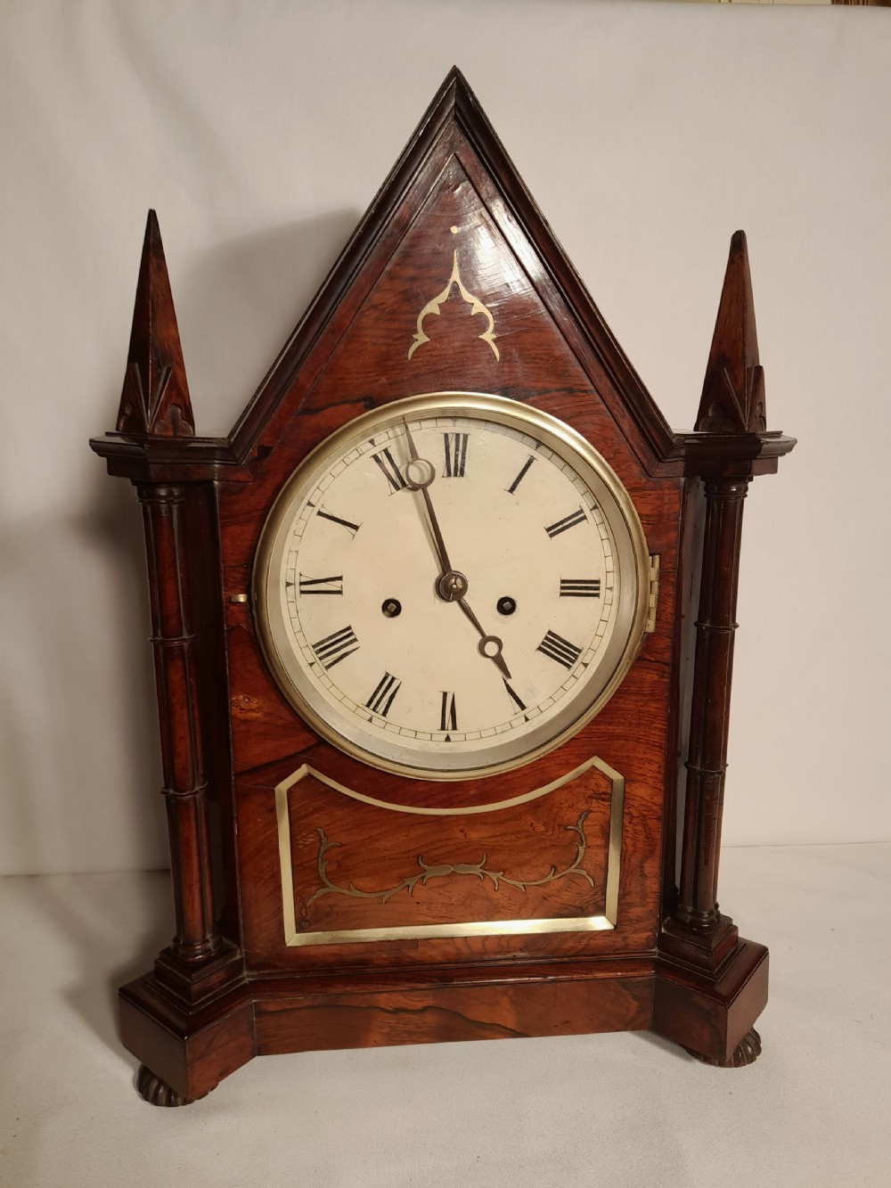 An antique Gothic Revival rosewood bracket clock with pointed arch pinnacles, brass foliate inlay, and a circular white dial with Roman numerals.