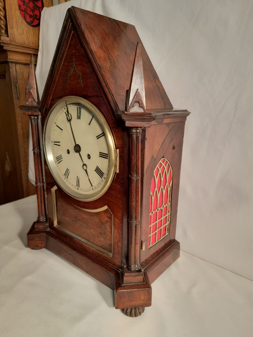 An antique Gothic Revival rosewood bracket clock with pointed arch pinnacles, brass foliate inlay, and a circular white dial with Roman numerals. View II
