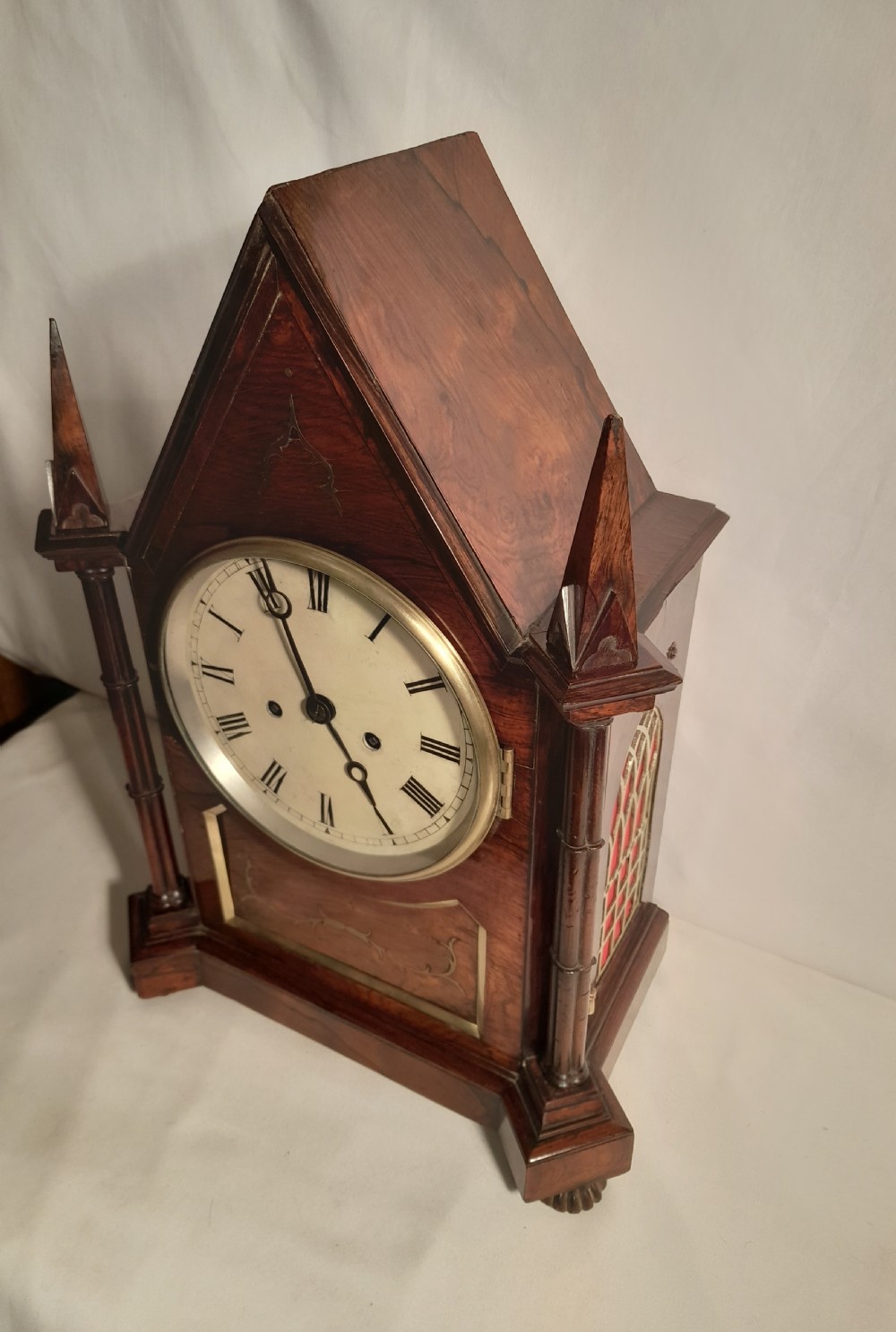 An antique Gothic Revival rosewood bracket clock with pointed arch pinnacles, brass foliate inlay, and a circular white dial with Roman numerals. View V