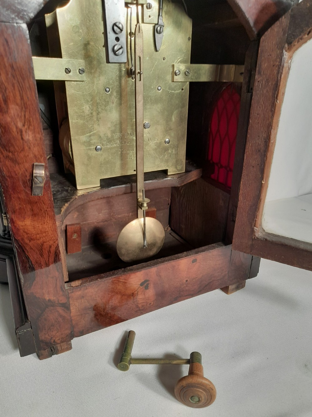 An antique Gothic Revival rosewood bracket clock with pointed arch pinnacles, brass foliate inlay, and a circular white dial with Roman numerals. View VI