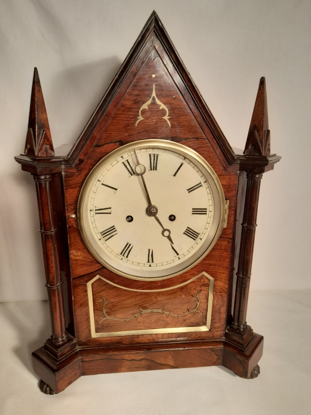 An antique Gothic Revival rosewood bracket clock with pointed arch pinnacles, brass foliate inlay, and a circular white dial with Roman numerals. View VIII