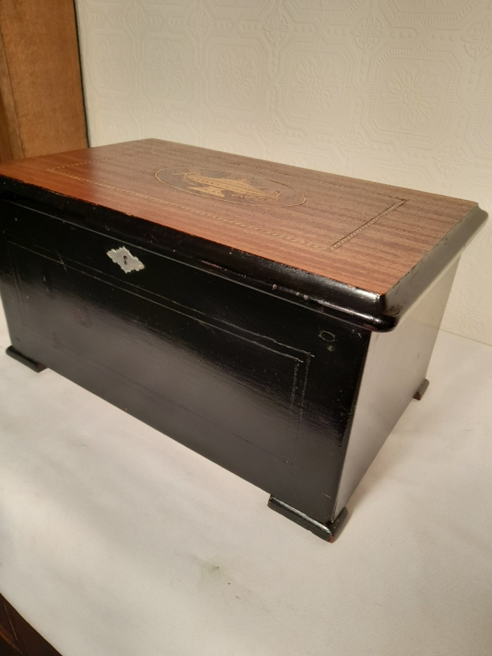An antique wooden music box with an ebonised lower case, a mahogany hinged lid featuring a marquetry urn inlay, and a central keyhole. View II