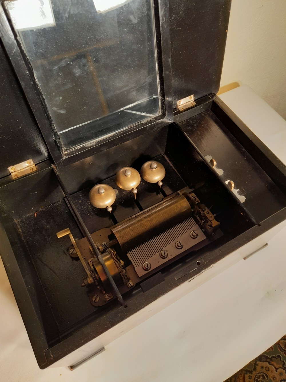 An antique wooden music box with an ebonised lower case, a mahogany hinged lid featuring a marquetry urn inlay, and a central keyhole. View V
