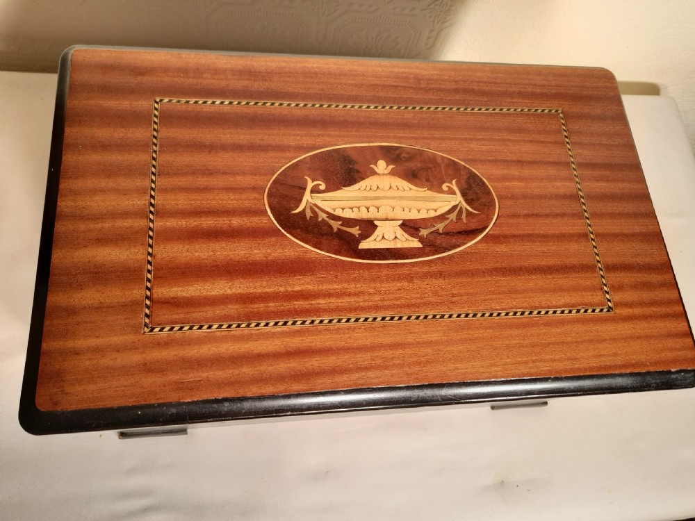 An antique wooden music box with an ebonised lower case, a mahogany hinged lid featuring a marquetry urn inlay, and a central keyhole. View VIII