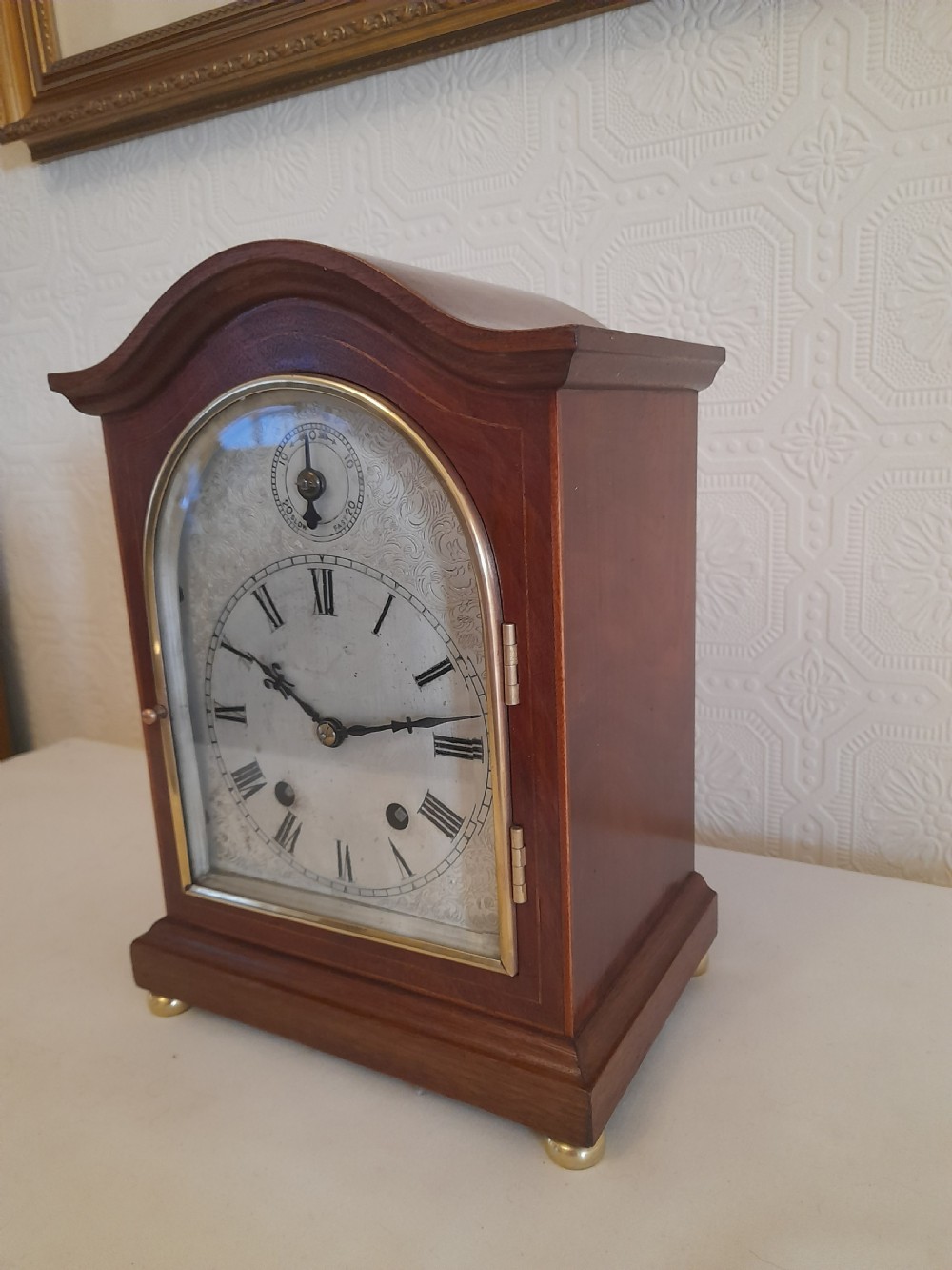 An arched mahogany wooden bracket clock with a silvered brass dial displaying Roman numerals and a small regulating dial at the top. View II