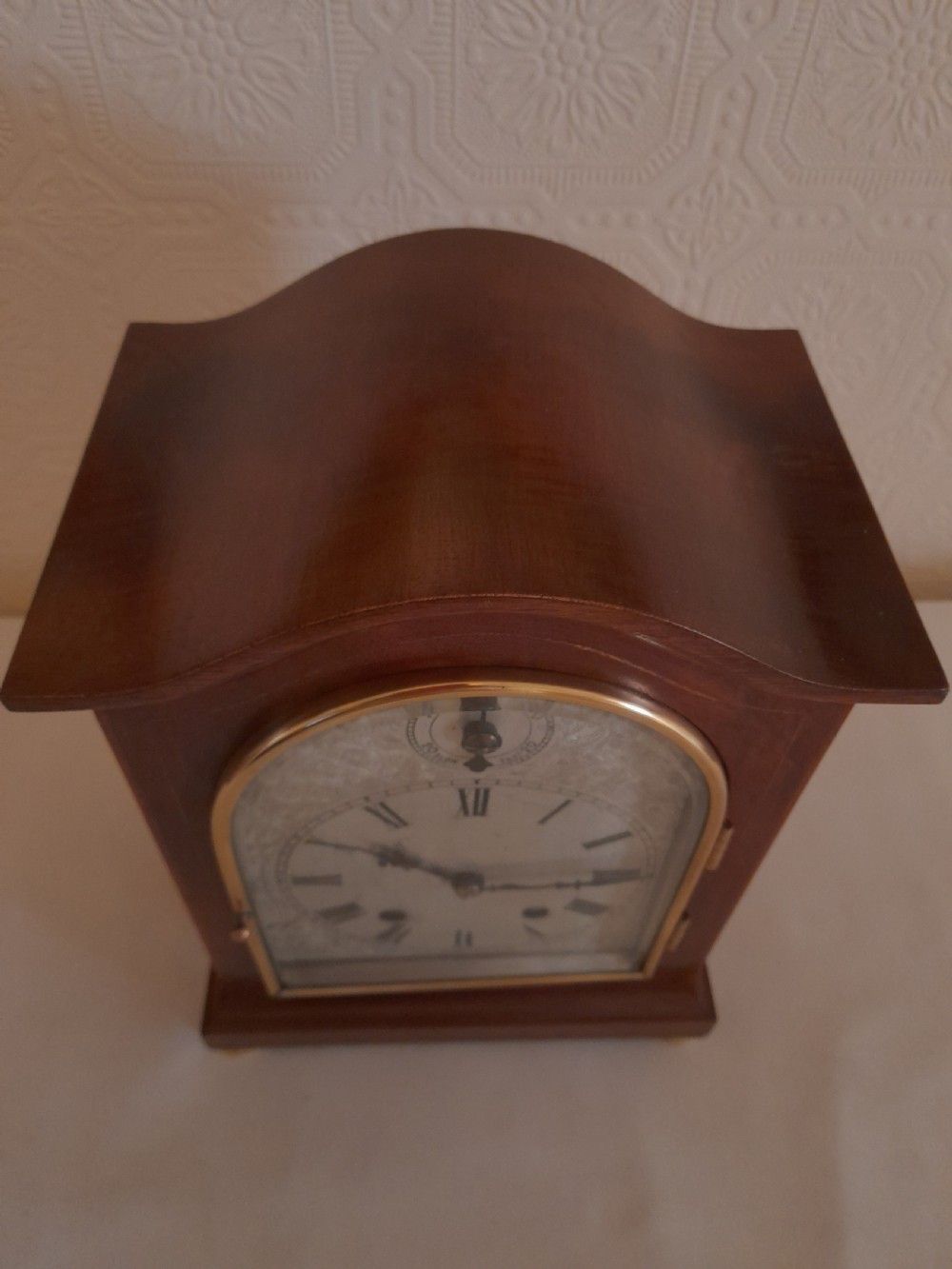 An arched mahogany wooden bracket clock with a silvered brass dial displaying Roman numerals and a small regulating dial at the top. View V