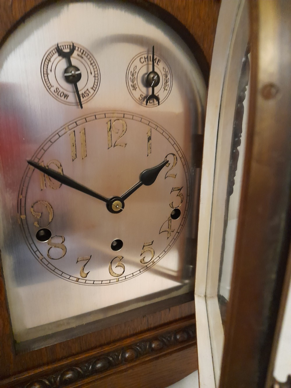 An Edwardian carved oak bracket clock featuring a silvered dial, brass bezel, arch top scroll moulding, and Westminster chime regulation sub-dials. View III
