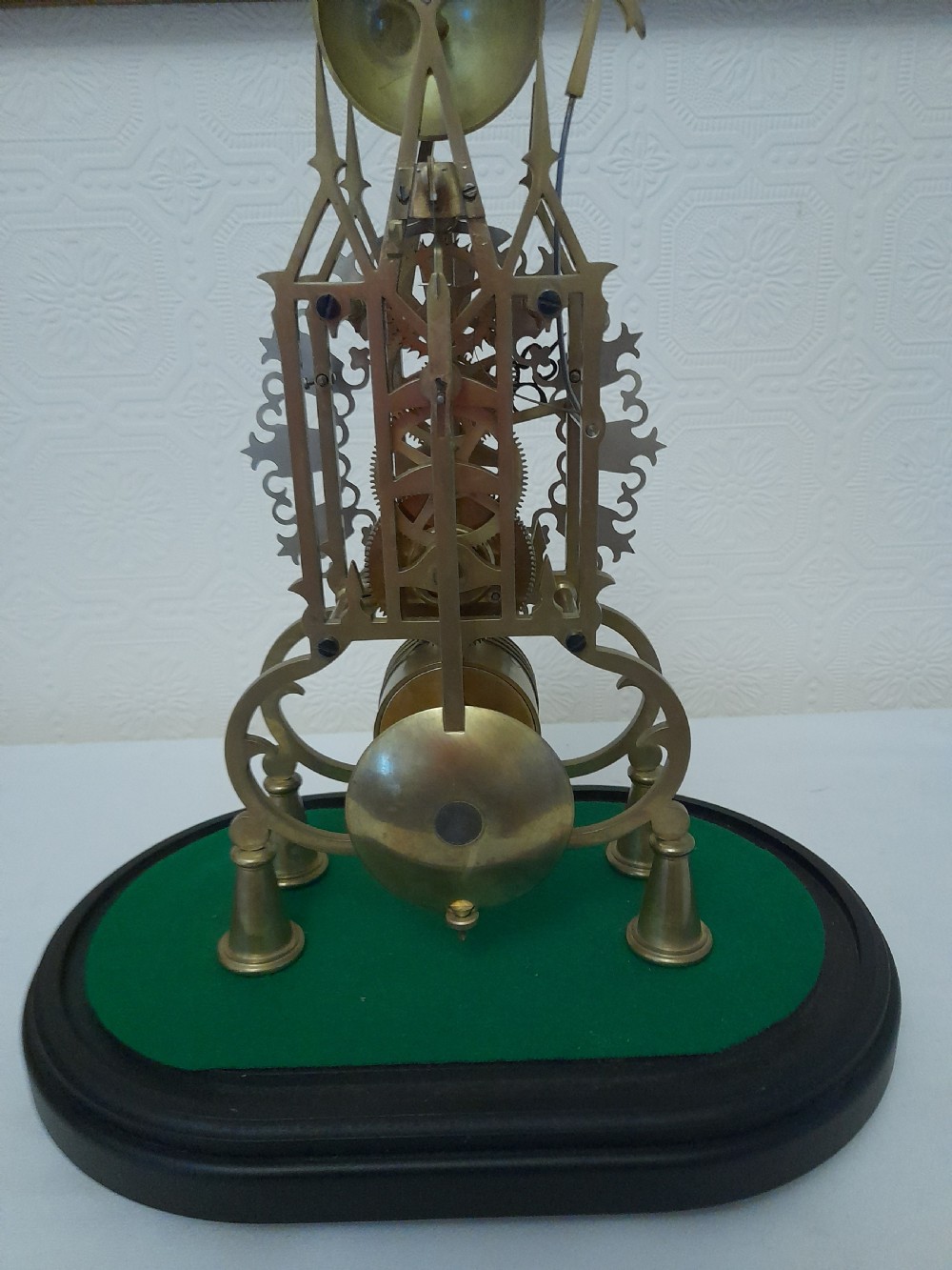A Victorian brass skeleton clock featuring exposed internal gears and a silvered Roman numeral dial, encased under a clear glass dome on an oval wooden base. View IV