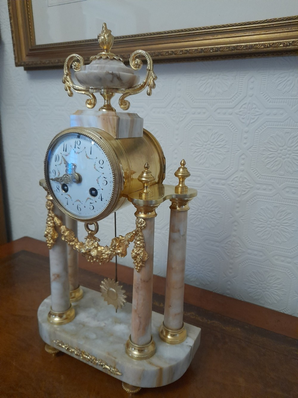 A French Louis XVI style marble and gilt brass portico mantel clock featuring four columns, floral swags, an urn finial, and an enamel dial.