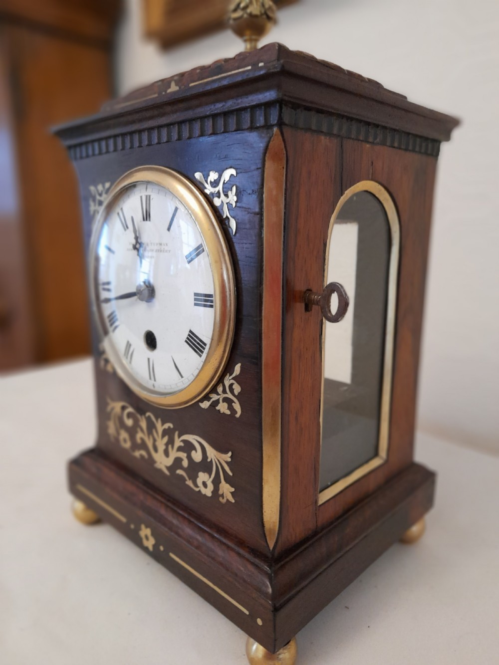 A Regency dark wood mantel clock featuring floral brass inlays, a white circular dial with Roman numerals, brass ball feet, and a top finial. View III
