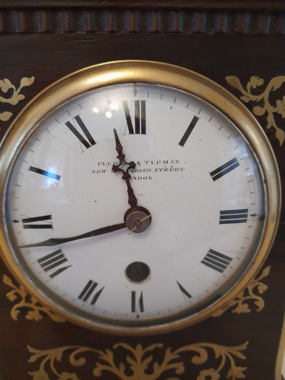 A Regency dark wood mantel clock featuring floral brass inlays, a white circular dial with Roman numerals, brass ball feet, and a top finial. View V