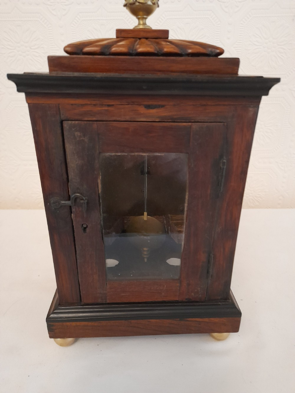 A Regency dark wood mantel clock featuring floral brass inlays, a white circular dial with Roman numerals, brass ball feet, and a top finial. View VII