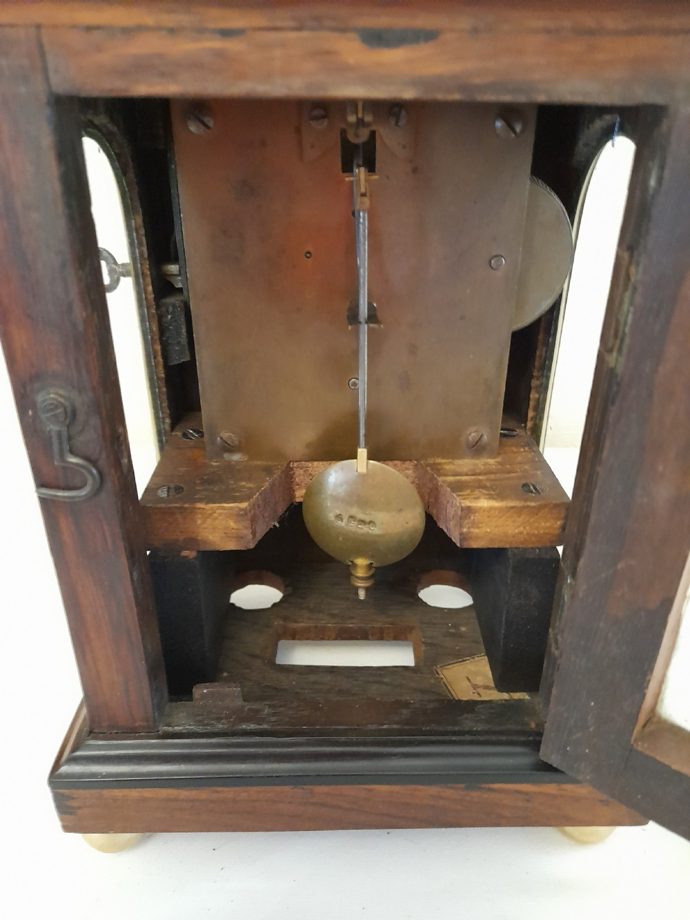 A Regency dark wood mantel clock featuring floral brass inlays, a white circular dial with Roman numerals, brass ball feet, and a top finial. View VIII