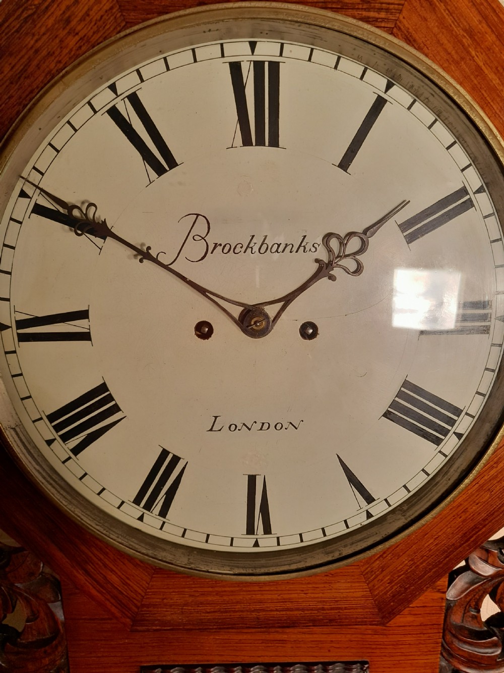 An antique mahogany drop-dial wall clock featuring an octagonal bezel frame, cream dial with Roman numerals, signature Brockbanks London, and carved side scrolls. View II